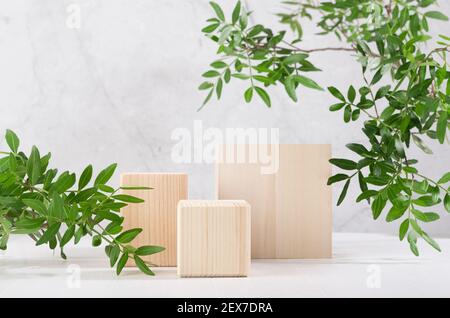 Naturstil für Kosmetik Produktdisplay - quadratische Holzpodien mit grünen Blättern, Schatten auf weißem Holztisch und graue Marmorwand. Stockfoto