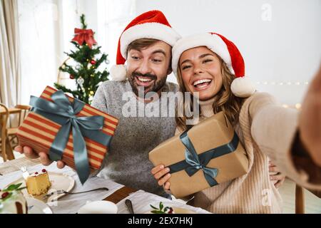 Nice aufgeregt paar unter Selfie mit Geschenkboxen während mit Weihnachtsessen im gemütlichen Zimmer Stockfoto