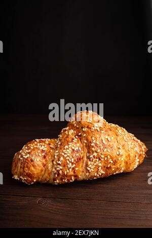 Croissant mit Sesam isoliert auf einem Holzhintergrund. Stockfoto