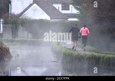 Loose Village, Kent, Großbritannien. Jogger, die an einem nebligen Morgen durch lockere Brooks auf dem Fußweg laufen Stockfoto