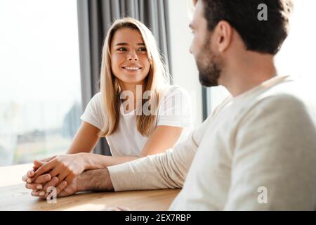 Junges Paar in der Liebe teilen einen zarten Moment klatschen Hände Während sie am Tisch sitzen und sich gegenseitig lächeln Augen Stockfoto