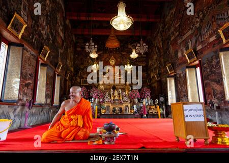 Ein Mönchspriester in orangefarbenen Gewändern sitzt im Tempelkomplex von Wat Arun in Bangkok. Stockfoto