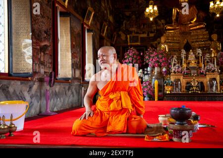 Ein Mönchspriester in orangefarbenen Gewändern sitzt im Tempelkomplex von Wat Arun in Bangkok. Stockfoto