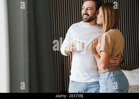 Glückliches junges Paar umarmt beim Stehen und mit Kaffee in Das Schlafzimmer Stockfoto