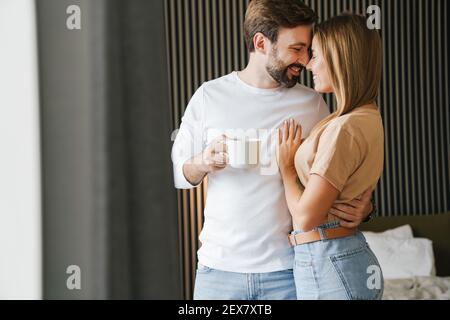 Glückliches junges Paar umarmt beim Stehen und mit Kaffee in Das Schlafzimmer Stockfoto