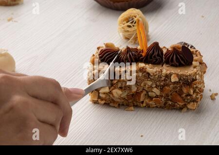 Hand mit Gabel Schneiden ein Stück Kuchen mit Walnuss mit Schokolade Dekoration gefüllt, Desserts in einem Studio Stockfoto