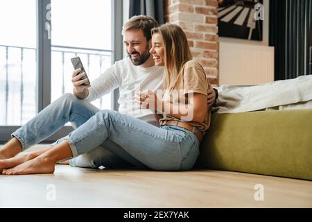 Glückliches schönes Paar mit Handy, während zu Hause entspannen Stockfoto