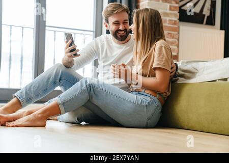 Glückliches schönes Paar mit Handy, während zu Hause entspannen Stockfoto