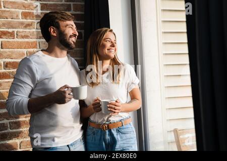 Glücklich junge attraktive Paar mit Kaffee, während an der stehen Fenster zu Hause Stockfoto