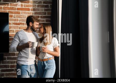Glücklich junge attraktive Paar mit Kaffee, während an der stehen Fenster zu Hause Stockfoto