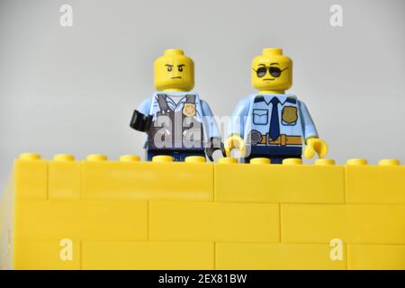 Zwei Polizisten Mini-Lego-Figuren hinter einer gelben Backsteinmauer aus Lego-Steinen gebaut Stockfoto