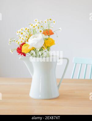 Bouquet von frischen Ranunculus Blumen und Gänseblümchen in einer mintgrünen Kaffeekanne aus dem Jahr 60ies und einem Stuhl in der gleichen Farbe und Design auf einem Holztisch. Stockfoto