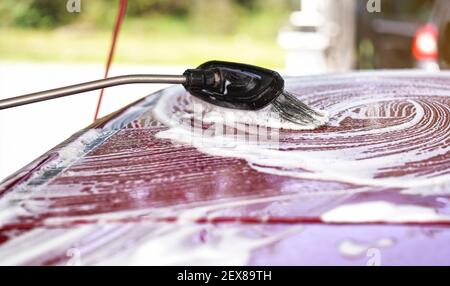 Pinsel hinterlässt Striche in weißem Shampoo und Schaum auf dem Dach des roten Autos gewaschen in Selbstbedienung Autowäsche. Stockfoto