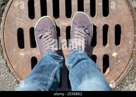Eine Frau Füße stehen an einem Sommertag auf der rostigen Metallabdeckung des Abwassers. Stockfoto