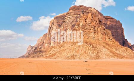 Großer Berg in roter Wüste, kleines 4WD Fahrzeug im Vordergrund für Maßstab - typische Landschaft von Wadi Rum, Jordanien Stockfoto