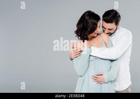 Mann küssen Schulter der schwangeren Frau isoliert auf grau Stockfoto