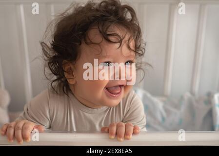 Nahaufnahme Porträt eines langhaarigen kleinen niedlichen Stillkind in einer Krippe stehen und lächeln. Stockfoto