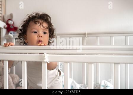 Porträt eines kleinen niedlichen nachdenklichen Stillkindlers, das in einer Krippe steht und nach vorne blickt. Stockfoto