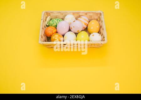 Ein gewebter Korb gefüllt mit bunten Ostereiern auf gelb Hintergrund Stockfoto
