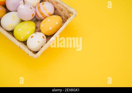 Ein gewebter Korb gefüllt mit bunten Ostereiern auf gelb Hintergrund Stockfoto