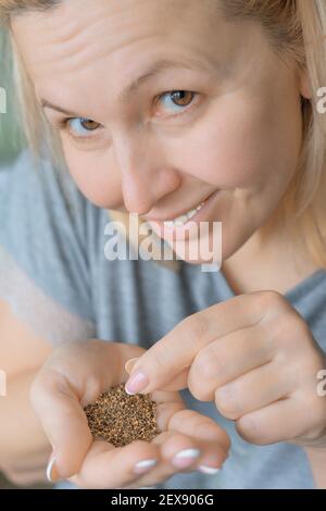 Gartenarbeit für zu Hause. Eine Erwachsene lächelnde kaukasische Frau hält Rucola-Samen in ihrer Handfläche. Vorbereitung für die Pflanzung von Rucola Samen. Micro-Green-Wachstum. Selektiver Fokus. Stockfoto