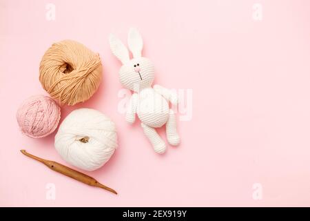 Weiße und braune Strickwolle, Hase Amigurumi und Häkelnadel auf rosa pastellfarbenem Hintergrund. Draufsicht, flach liegend, Kopierbereich Stockfoto