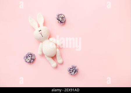 Gestrickter Hase Amigurumi mit Blüten isoliert auf einem rosa Hintergrund. Baby Hintergrund. Platz kopieren, Draufsicht. Stockfoto
