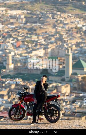 Ein junger Einheimischer posiert neben seinem Motorrad mit Blick auf das Stadtbild der Fes Medina, von den Mariniden Gräbern, Fes, Marokko aus gesehen Stockfoto