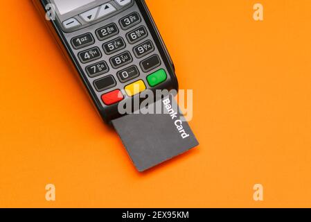Zahlungsterminal mit Kreditkarte. Modernes Gerät zur Bezahlung von Dienstleistungen und Waren auf orangefarbenem Hintergrund. Geld von einer Debitkarte abschreiben. Stockfoto