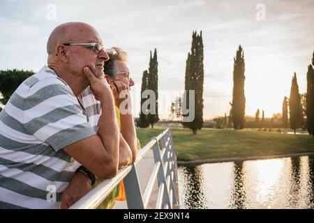 Rentnerpaar, das den Sonnenuntergang von einer Brücke aus beobachtet Stockfoto