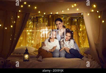 Porträt von glücklicher Mutter und kleinen Kindern lächeln an der Kamera Sitzen im gemütlichen Bettzelt Stockfoto