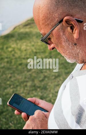 65-jähriger Mann schaut auf sein Smartphone in einem Park Stockfoto