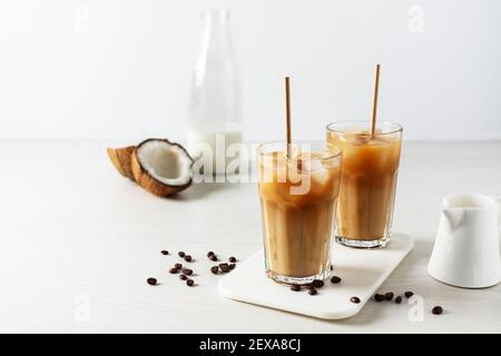 Eiskaffee mit Kokosmilch in einem hohen Glas auf weißem Holztisch. Kalte Erfrischung Sommergetränk. Stockfoto