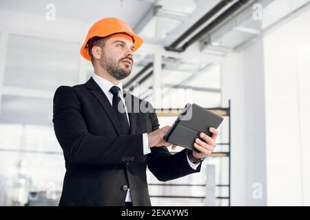 Fokussierter Mann in Anzug und Hardhat mit Tablet bei der Arbeit Stockfoto