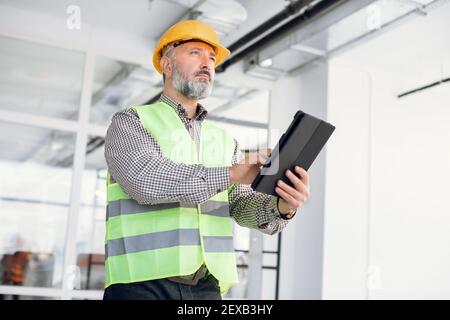 Reifer Inspektor in Hardhat arbeiten an Tablette auf Objekt Stockfoto