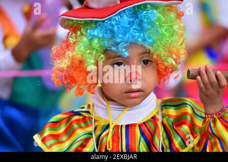 Lokales Kind mit einem Clown Gesicht Malerei und ein buntes Kostüm Teilnahme an der Parade Día de los Locos in San Miguel de Allende Guanajuato, Mexiko. Stockfoto