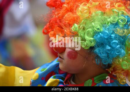 Lokales Kind mit einem Clown Gesicht Malerei und ein buntes Kostüm Teilnahme an der Parade Día de los Locos in San Miguel de Allende Guanajuato, Mexiko. Stockfoto