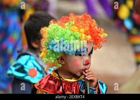 Lokales Kind mit einem Clown Gesicht Malerei und ein buntes Kostüm Teilnahme an der Parade Día de los Locos in San Miguel de Allende Guanajuato, Mexiko. Stockfoto