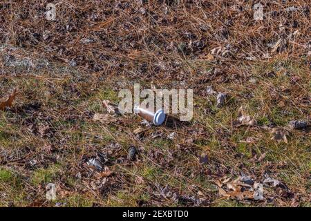 Eine Papiertasse mit Kaffee und Plastikdeckel entsorgt Auf dem Boden achtlos im Park die Umwelt verschmutzen Stockfoto