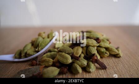 Trockene Kardamom Schoten auf einem hölzernen Hintergrund setzen. Frische Elaichi (Elettaria cardamomum) Gewürze Haufen mit weißem Löffel in der Küche. Indische Gewürze Stockfoto