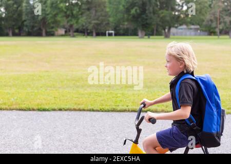 Kleines Kind, das auf dem Fahrrad zur Schule geht. Schüler mit Fahrrad auf dem Schulhof. Schulfußballplatz und ein Junge auf dem Fahrrad. Stockfoto