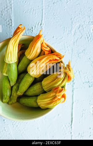 Frische Zucchini-Blüten mit anhängenden Baby-Zucchini in einer pastellgrünen Schale auf einer hellblauen verzweifelten Oberfläche. Stockfoto