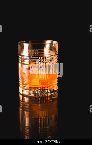 Ein altmodischer Cocktail in einem Steinglas, das auf der schwarzen reflektierenden Oberfläche einer Feuerstelle im Freien sitzt. Stockfoto