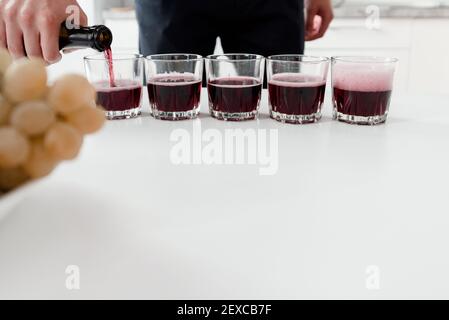 Der Barkeeper gießt Rotwein in Gläser auf dem weißen Tisch. Roter hausgemachter Wein in Gläsern. Stockfoto