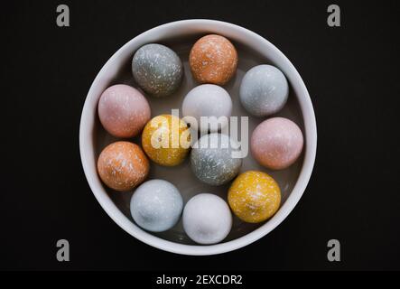 Bunte Ostereier in weißer Schale auf schwarzem Hintergrund Stockfoto