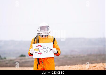 Mann als Astronaut gekleidet hält ein Plakat mit einem Zeichnung einer Rakete Stockfoto