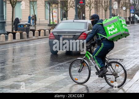 Fahrer mit Fahrrad und Maske unter dem Regen arbeitet für Bolt Food, Online-Food-Bestellung und Lieferservice, die Bestellungen über eine mobile App nimmt Stockfoto