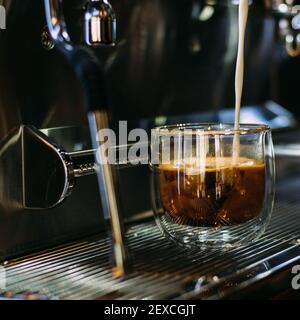 Milch in eine Glastasse mit Kaffee gießen Stockfoto