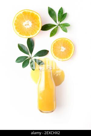 Eine Flasche frischen Orangensaft liegt in einer Pfütze mit Orangenstücken und Blättern auf weißem Hintergrund, Nahaufnahme, Draufsicht. Stockfoto