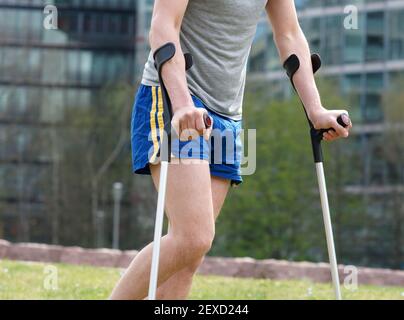 Junger Mann in Sportkleidung Spaziergänge in Stadtpark mit Krücken Nach Sportunfall Stockfoto